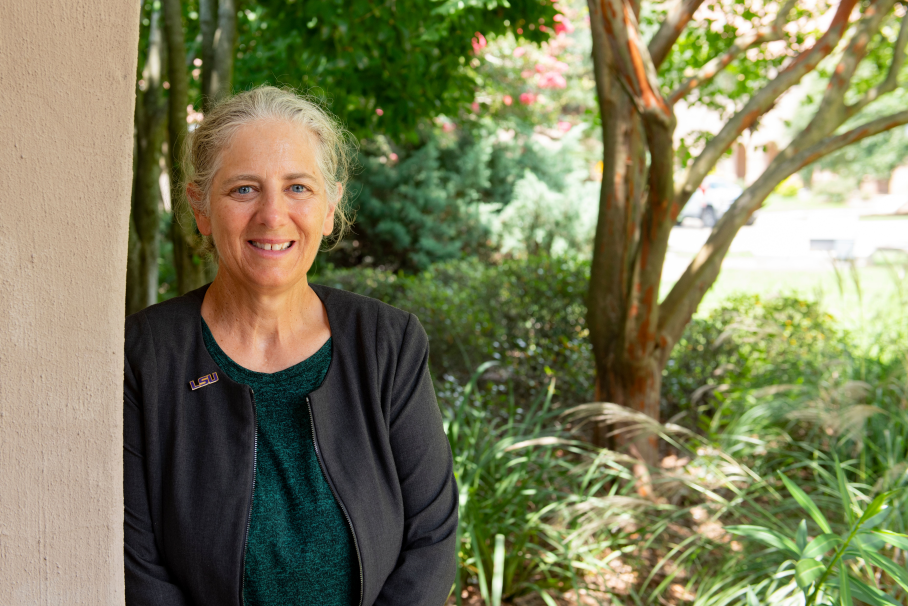 photo of marybeth lima standing against a wall with trees in the background.