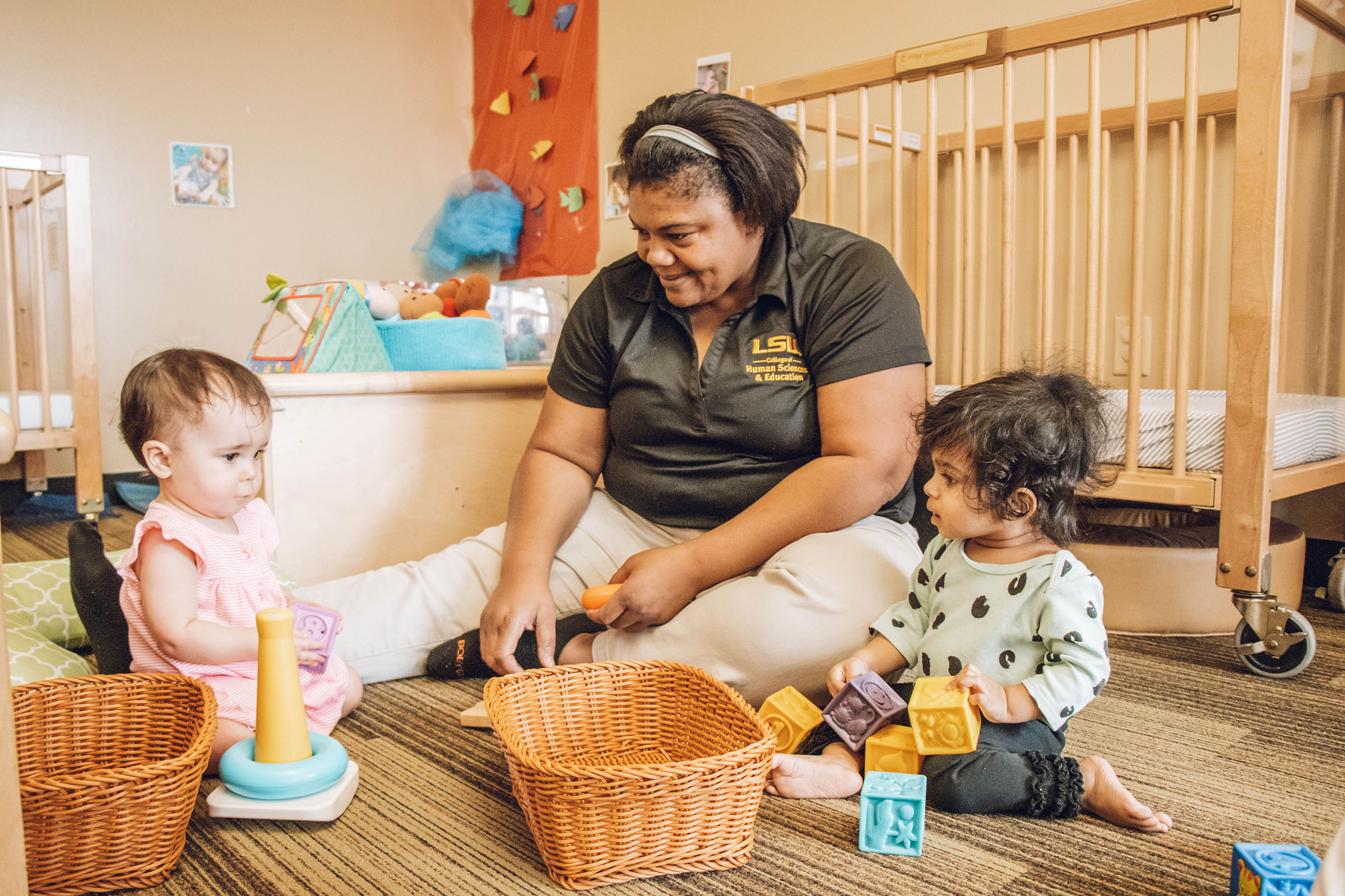 Black female teacher playing on the floor with two female young toddlers