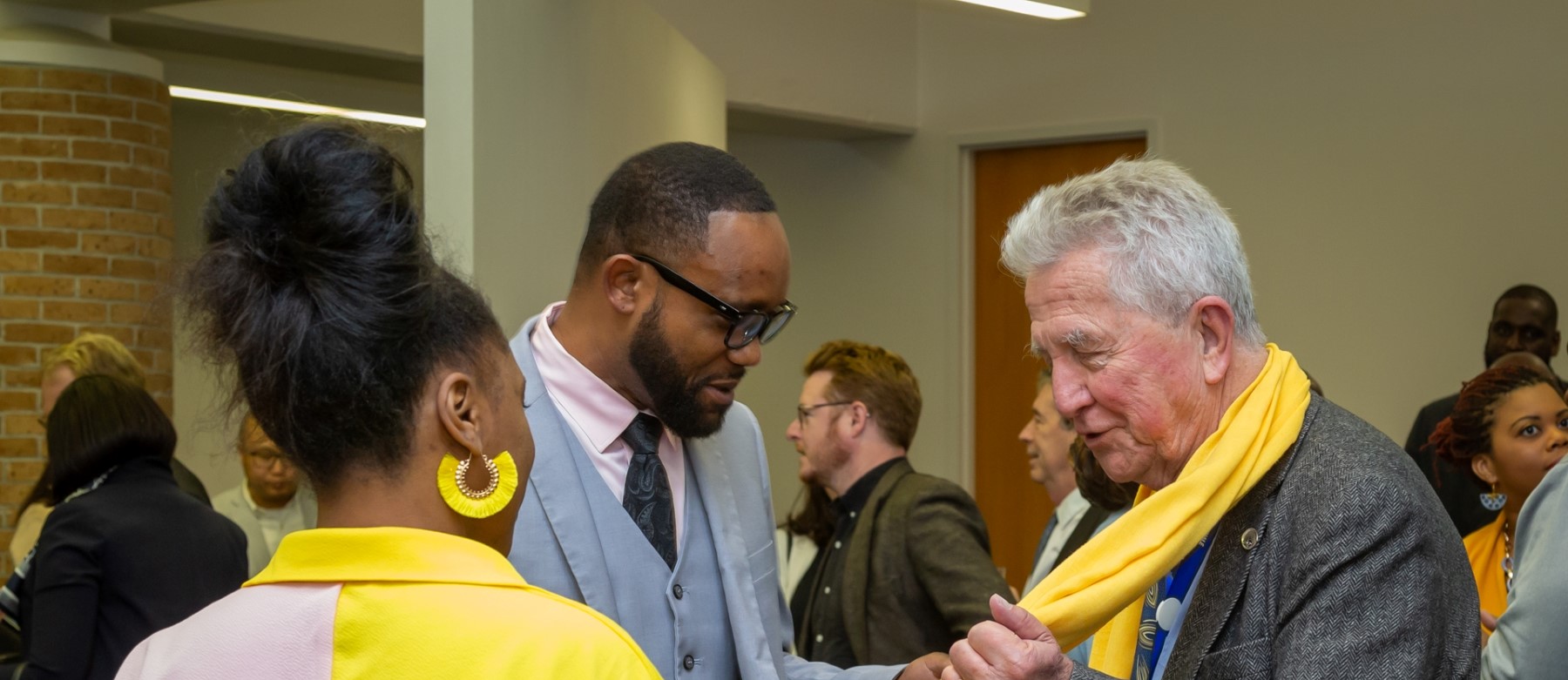 three people stand in a crowded room and talk